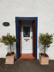 a door with two potted trees in front of a building at Kirk Cottage in Tobermory