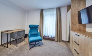 Zimmer mit einem blauen Stuhl, einem Schreibtisch und einem TV in der Unterkunft Hotel Reiler Hof in Reil