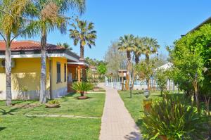 a yellow house with palm trees and a sidewalk at Villaggio Selene Mare in Paestum