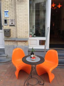 2 orangefarbene Stühle sowie ein schwarzer Tisch und Stühle in der Unterkunft B&B Geste d' Alice in Westende