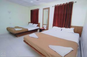 two beds in a room with red curtains at Rajhuns Deluxe Lodging in Kolhapur