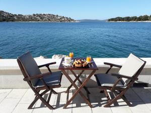 Deux chaises et une table avec de la nourriture à côté de l'eau dans l'établissement Sea Star, à Tribunj