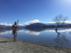 Ein Mann, der neben einem See steht und eine Fledermaus hält. in der Unterkunft WanaHaka - Lake Wanaka & Town at your door in Wanaka
