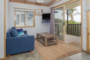 a living room with a blue couch and a balcony at Tuross Beach Cabins & Campsites in Tuross Heads