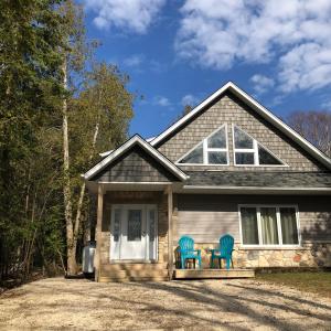 a house with two blue chairs on the front porch at The Whippoorwill Cottage - NBP-2022-201 in Lion's Head