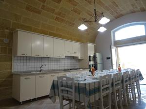 a kitchen with a long table with white cabinets and chairs at Dimora Rizzo con tappeti di pietra in Leuca