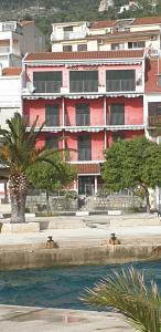 a red building with a palm tree in front of it at Casa Rosada in Podgora