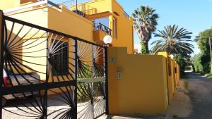 a yellow house with a fence and palm trees at Villa Asmara in Su Forti