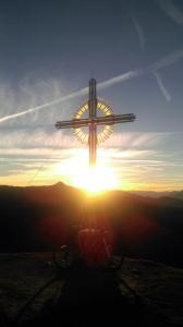 a cross on top of a hill with the sunset at Holzfällerhaus Melkstatt in Auffach