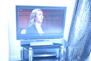 a television on a stand with a woman on the screen at Regent Guest House in Grimsby