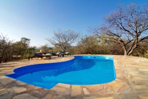 a blue swimming pool with a table and trees at Ohange Namibia Lodge in Otavi