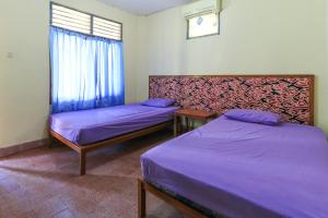 two beds in a room with purple sheets and a window at Mertha Jati Hotel in Kuta