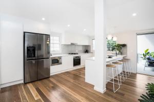 La cuisine est équipée de placards blancs et d'un réfrigérateur en acier inoxydable. dans l'établissement Park Avenue Terrace House Sleeps 9, à Brisbane