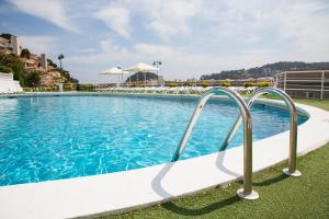 a large swimming pool with blue water and metal rails at Hotel - Bungalows Don Juan Tossa in Tossa de Mar