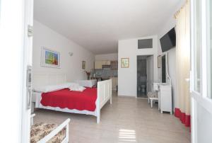 a white bedroom with a red bed and a kitchen at Apartments Coce in Trogir