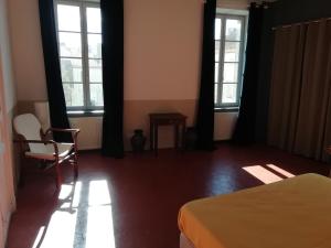 1 dormitorio con 2 ventanas, 1 cama y 1 silla en Les Colonnades, en Moussan
