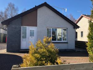 una casa con una puerta blanca y algunos arbustos en Linmore, en Aviemore