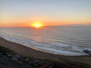 a sunset over a beach with the ocean at Hightide Apartment in Amanzimtoti