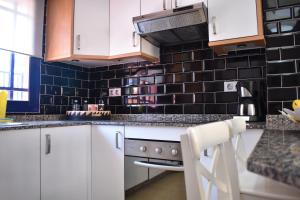 una cocina con armarios blancos y azulejos negros en la pared en TC Tríplex Bahía Meloneras en Meloneras