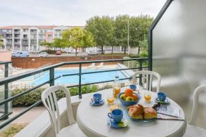 una mesa con desayuno en el balcón con vistas a la piscina en Vacancéole - Les Jardins de l'Amirauté, en Les Sables-dʼOlonne