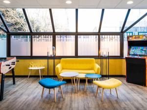 Habitación con sofá amarillo, mesas y ventanas en Ibis Styles Paris Saint Denis La Plaine, en Saint-Denis