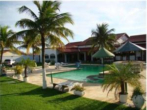 a swimming pool with palm trees in front of a building at Pousada La Maison in Iguaba Grande