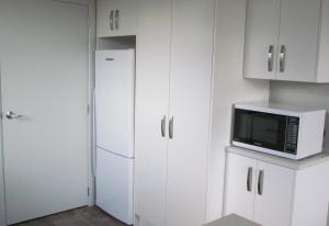 a kitchen with white cabinets and a microwave and a refrigerator at Birchwood Cottages in Te Anau