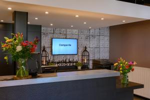 a waiting room with a tv on a wall with flowers at Campanile Hotel & Restaurant Eindhoven in Eindhoven