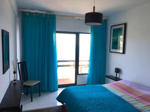 a bedroom with blue curtains and a bed and a window at Chuva De Prata in Caniço