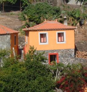 an orange house with red windows on a stone wall at Madeira-Meerblick-Haus in Estreito da Calheta