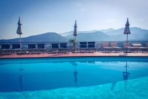 a swimming pool with chairs and umbrellas and mountains at Hotel Cristina in Sorrento