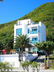 a white building with a hill in the background at Muxia Siji Sea View Guesthouse in Yanliau