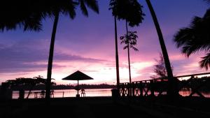 a sunset over a beach with palm trees and the ocean at Salty Dog Hostel in Telukdalem