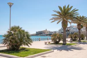 a row of palm trees on a sidewalk near the water at Opera Dimore in Vieste