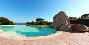 a swimming pool with a rock next to the ocean at Hotel Punta Negra in Alghero