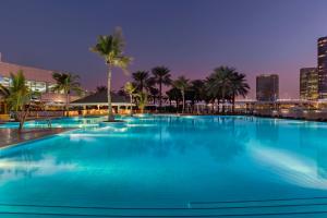 a large swimming pool with palm trees and a city skyline at Beach Rotana Residences in Abu Dhabi