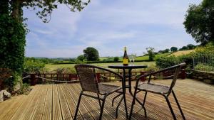 a table and chairs on a wooden deck with a bottle of wine at Ty Doli Cottage, rural location just outside Conwy town in Llangelynin