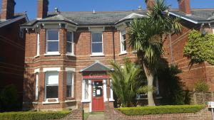 ein Backsteinhaus mit einer roten Tür und einer Palme in der Unterkunft Colebrook Guest House in Farnborough