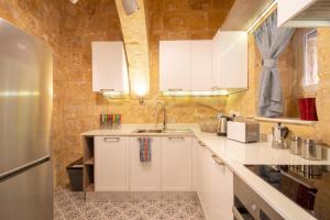 - une cuisine avec des placards blancs et un mur en pierre dans l'établissement 16 lettings - charming character house, à Il-Birgu