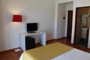 a room with a bed and a desk with a television at Guest House - Duna Parque Group in Vila Nova de Milfontes