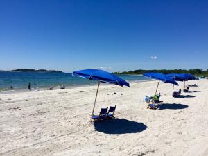 a row of blue beach chairs and umbrellas on a beach at Inn By the Sea in Cape Elizabeth