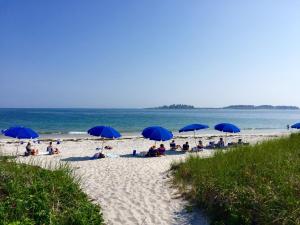 a group of people sitting under blue umbrellas on a beach at Inn By the Sea in Cape Elizabeth