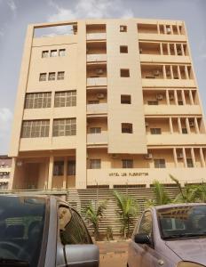 un gran edificio con coches estacionados frente a él en Hotel Les Fleurettes, en Ouagadougou