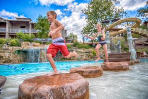 a boy and a girl jumping on a rock in a pool at Still Waters Resort in Branson