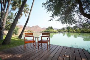 two chairs and a table on a wooden deck near a lake at Omarunga Epupa-Falls Camp in Epupa +9 photos