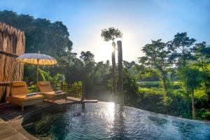 a swimming pool with an umbrella and two chairs and a fountain at Alam Dania Cottage in Ubud