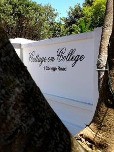 un cartello per una strada universitaria dietro due alberi di Cottage on College a St Francis Bay