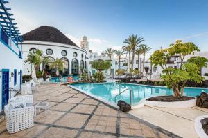 a pool at a resort with palm trees and a building at Hotel LIVVO Volcán Lanzarote in Playa Blanca