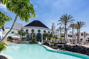 a pool at a resort with palm trees and a building at Hotel LIVVO Volcán Lanzarote in Playa Blanca