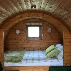 Cama pequeña en una cabaña de madera con ventana en Rivendell Glamping Pods, en Holsworthy